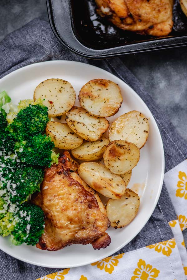 potatoes and baked chicken with a side of stovetop broccoli on a white plate.