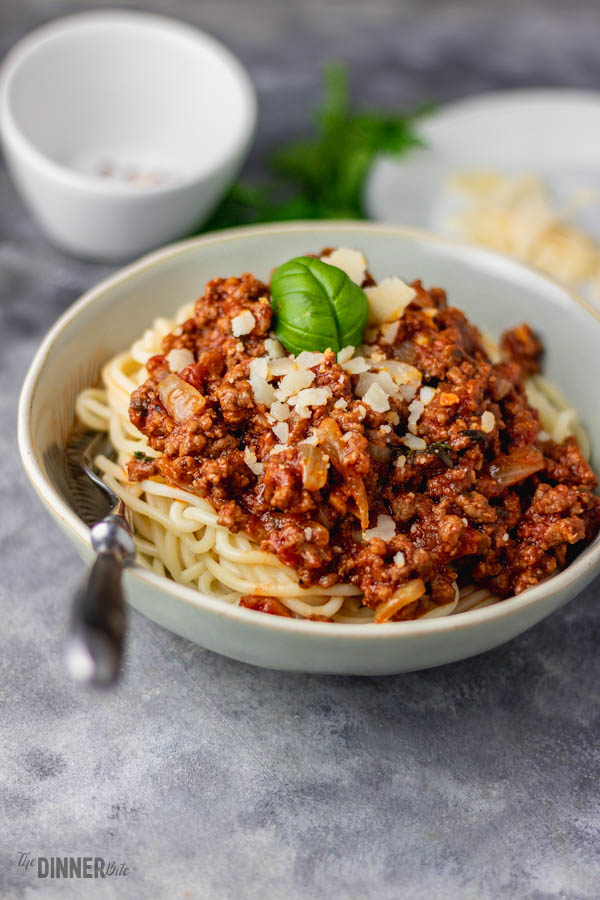 a bowl of spaghetti and beef sauce with cheese and fresh basil.