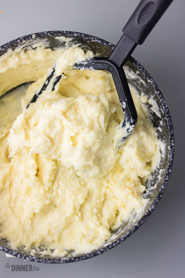creamy garlic mashed potatoes with potato masher in a saucepan.