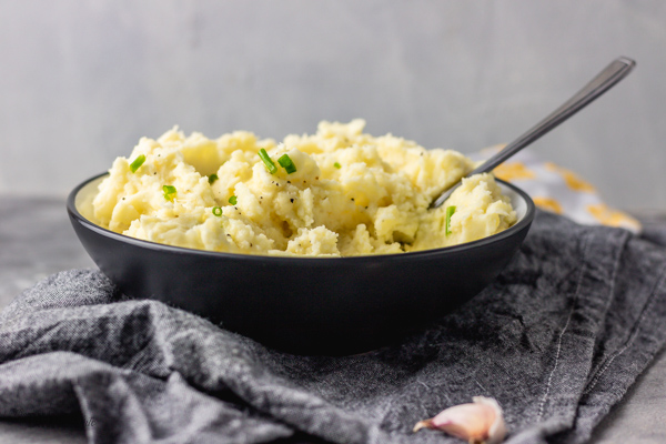 creamy garlic mashed potatoes in a bowl garnished with melted butter and chopped chives.