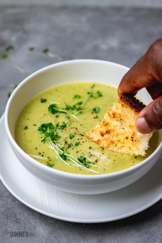 a hand of a man dipping crusty bread into broccoli soup. 