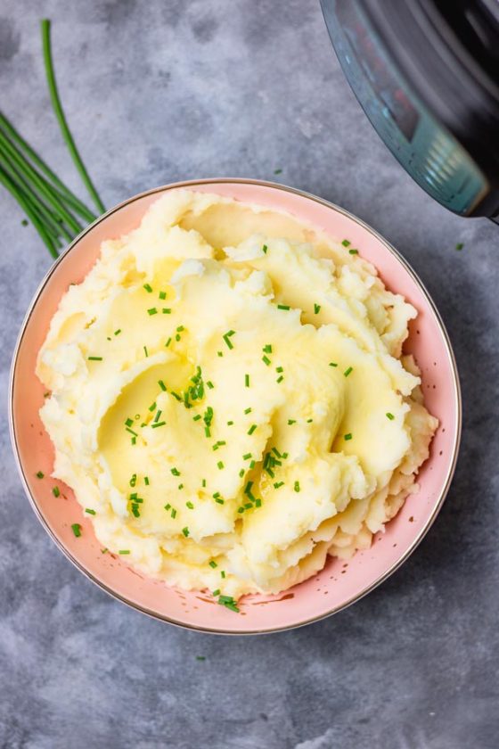 instant pot mashed potatoes in a pink bowl. mashed potatoes garnished with chopped chives and melted butter