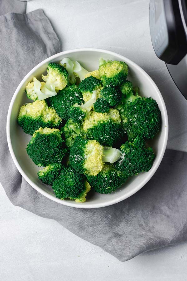 instant pot pressure cooker broccoli in a bowl placed on a grey napkin.