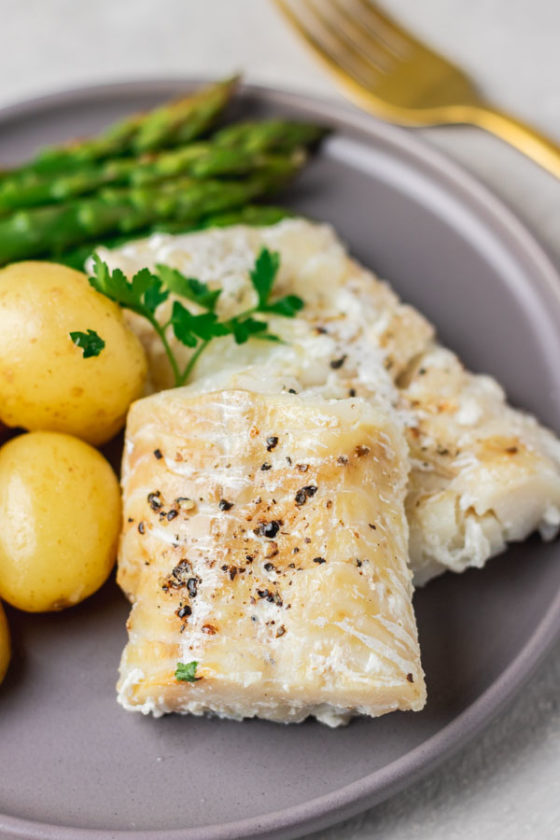 a plate containing steamed cod fish, potatoes and asparagus.