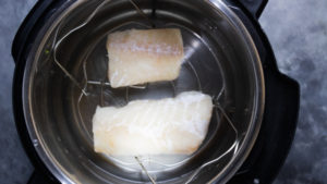 two frozen cod fish on a trivet in an instant pot.