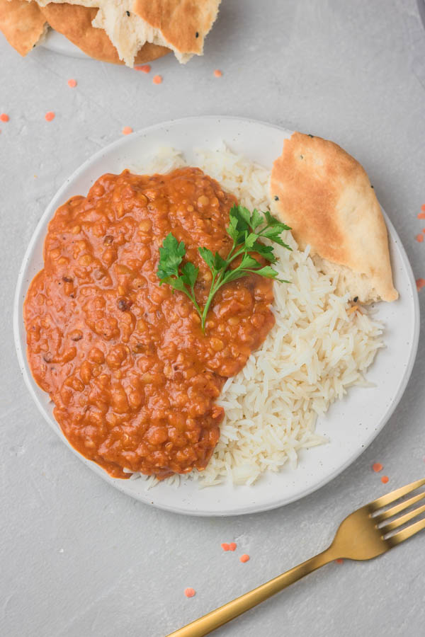 a plate of lentil curry and basmati rice with a small side of naan bread.