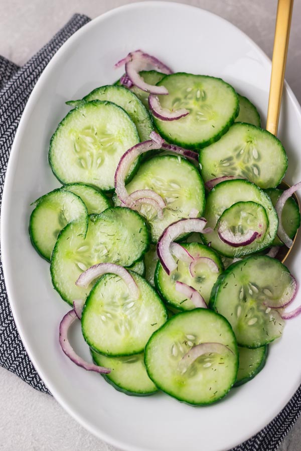 cucumber salad with chopped onions in an oval bowl with a serving spoon..