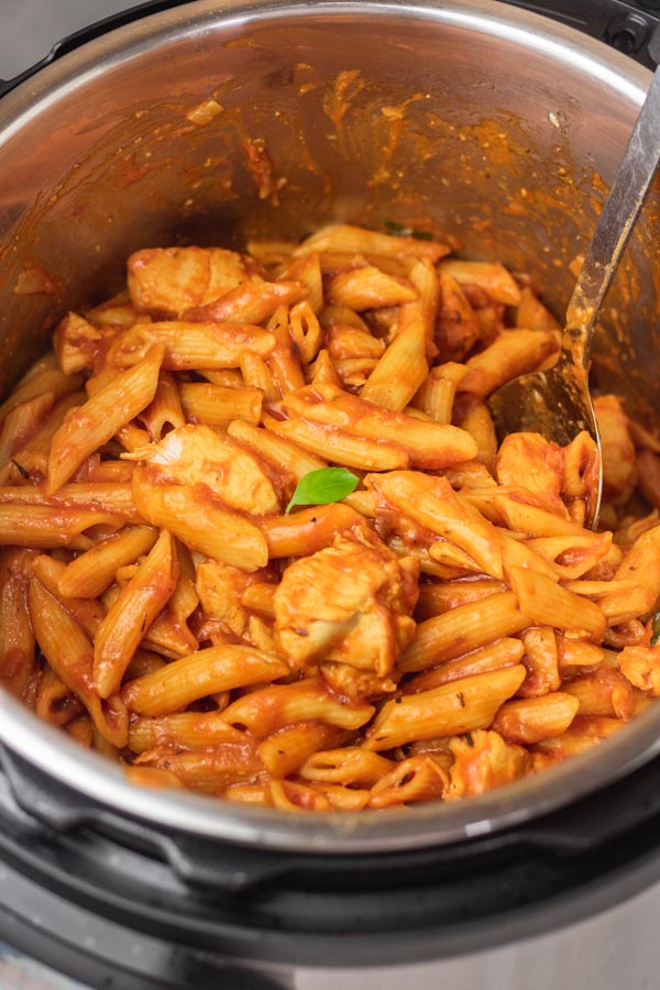 a serving spoon in a pot of pasta and chicken.