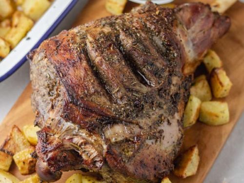 roasted leg of lamb on a wooden board with some cubed potatoes.