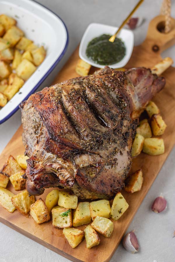 roasted leg of lamb on a wooden board with some cubed potatoes.