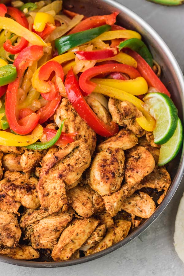 a pan of chicken jajitas and peppers with lime slices. 