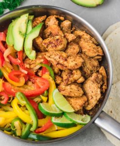 a skillet of cooked chicken breats strips and sauteed peppers with avocado slices.