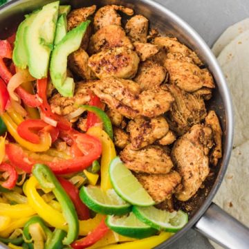 a skillet of cooked chicken breats strips and sauteed peppers with avocado slices.