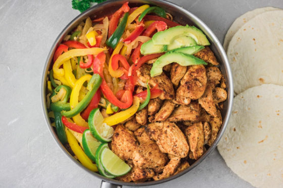 a skillet of chicken fajitas and tortilla wraps on the side.