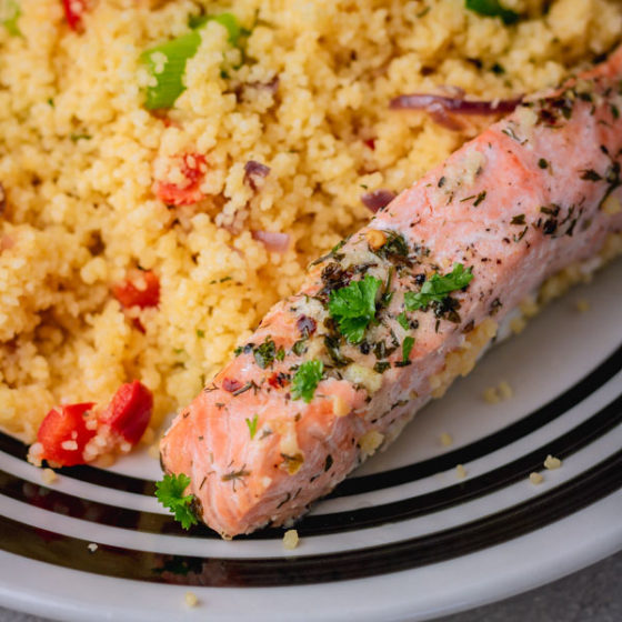 a plate of vegetable couscous and baked salmon fillet garnished with chopped parsley.