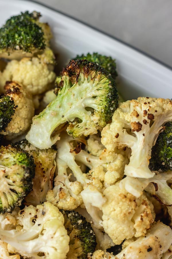 roasted cauliflower and broccoli in a white and silver enamel baking dish.