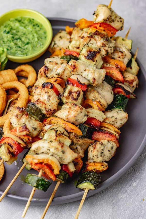chicken skewers on a grey plate with french fries and green dip.