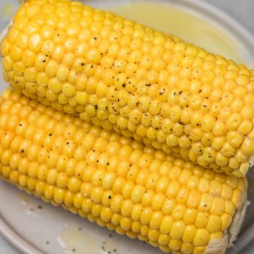 two ears of corn season with salt and pepper on a plate.