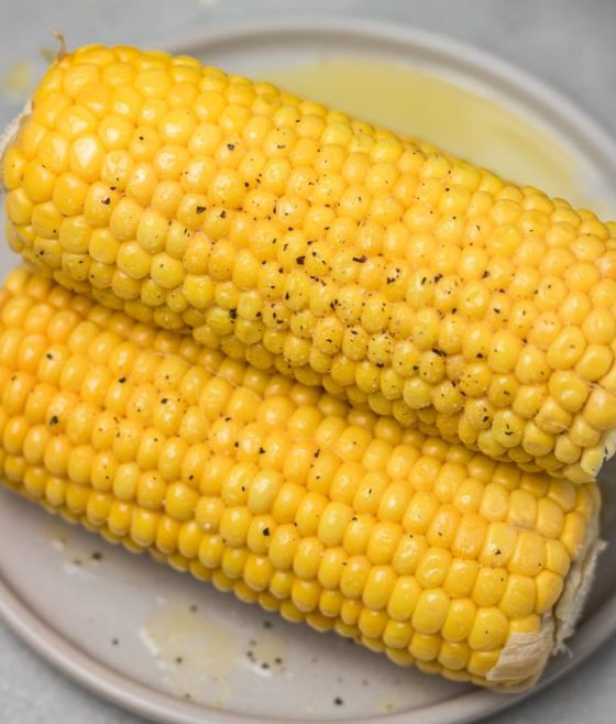 two ears of corn season with salt and pepper on a plate.
