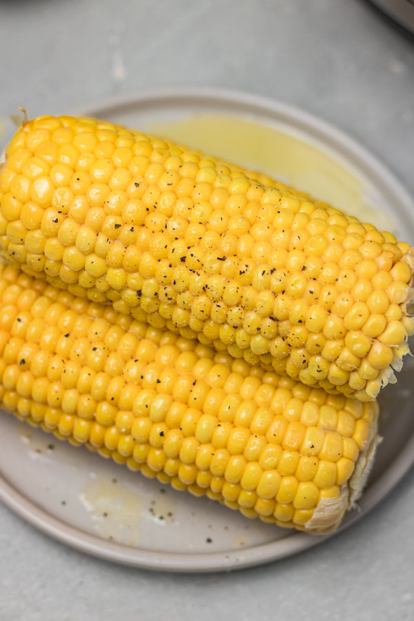 stack of cooked corn on a plate with a drizzle of melted butter.
