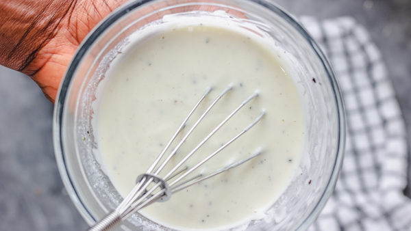 a bowl of creamy dressing and a whisk.