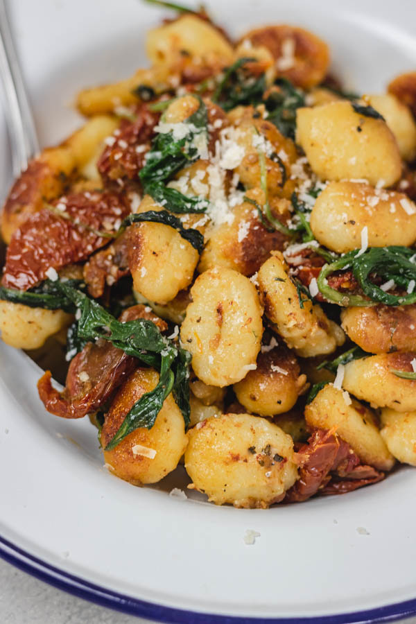 a plate of pan fried gnocchi with spinach and sun dried tomatoes with a sprinkle of cheese.