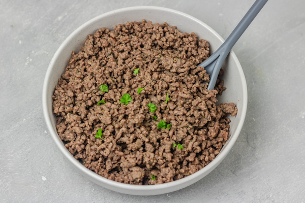 a bowl of ground beef garnished with parsley.