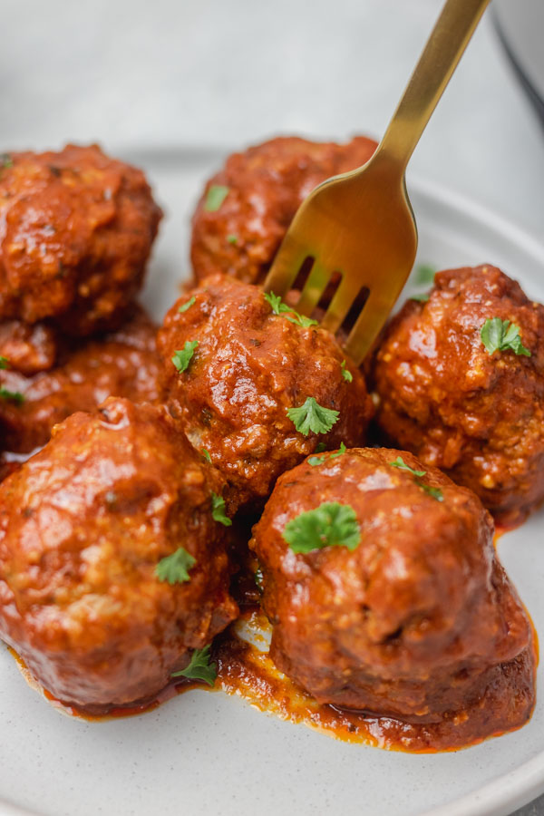fork holding a meatball covered in tomato sauce.