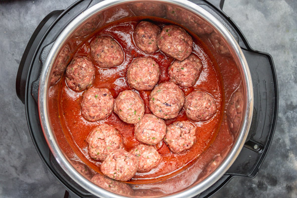 raw meatballs and sauce in a pressure cooker.
