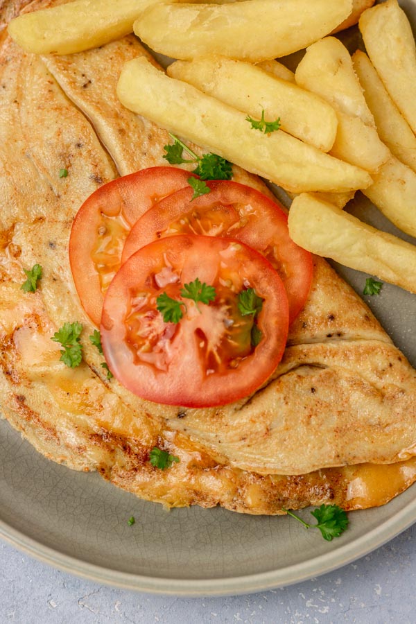 omelette topped with sliced tomatoes with the side of chips.