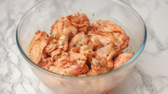 seasoned uncooked chicken wings in a glass bowl.