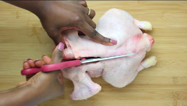a hand with a scissors cutting through the backbone of a chicken.