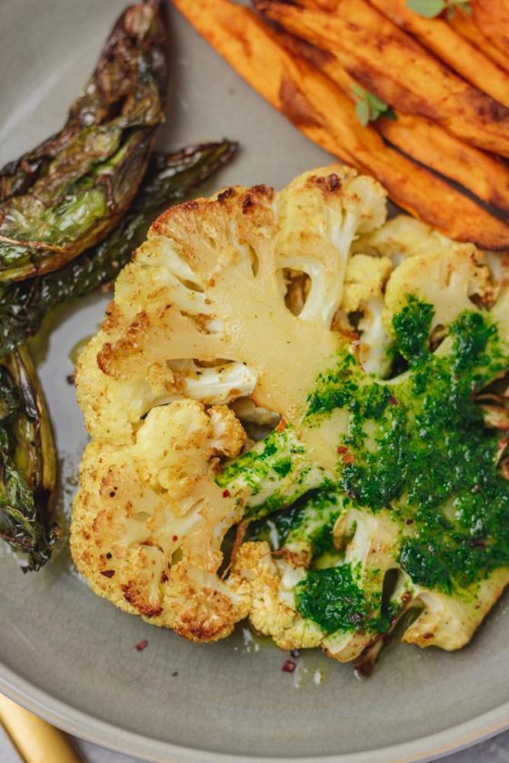 cauliflower steak covered with green sauce on a plate with sweet potato fries.