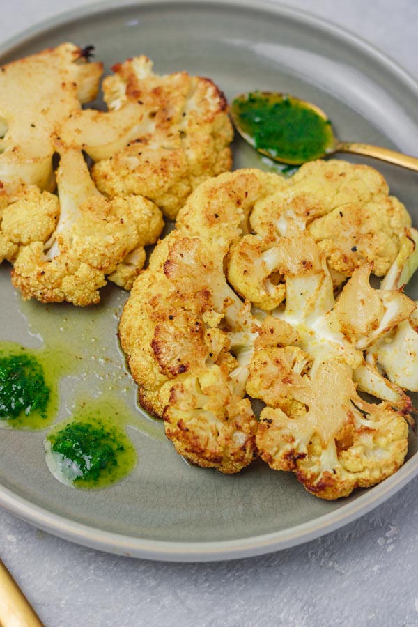 two cauliflower steaks on a plate with green sauce.