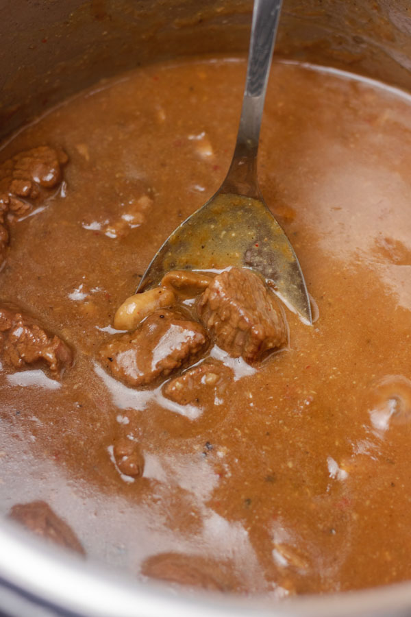 a pot of gravy and beef in a ladle.