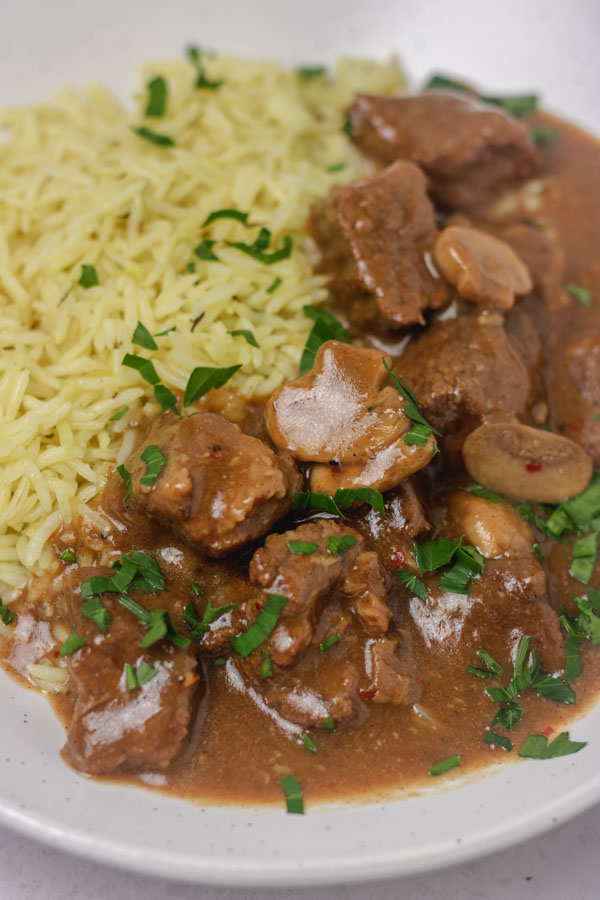 beef and mushroom gravy with rice in a specked cream plate.