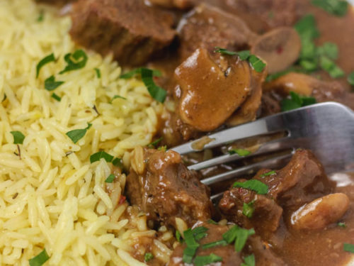 a plate of rice and beef with gravy garnished with chopped parsley.