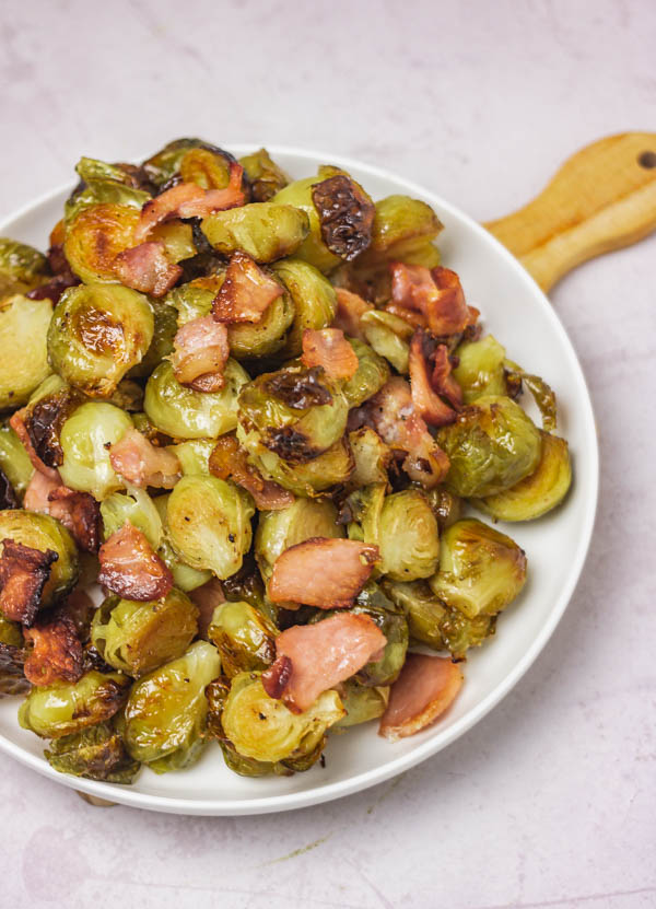 a close of roasted brussels sprouts and bacon in a white side plate.
