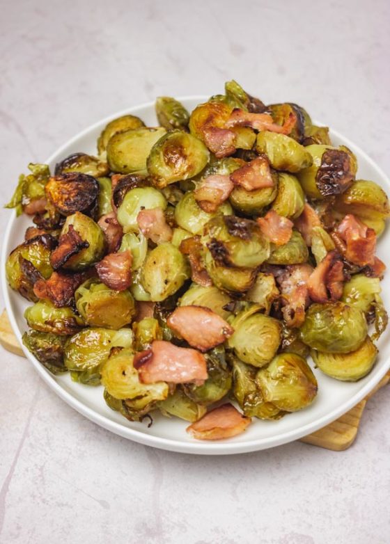 brussels sprouts and bacon on a white side dish placed on a board.