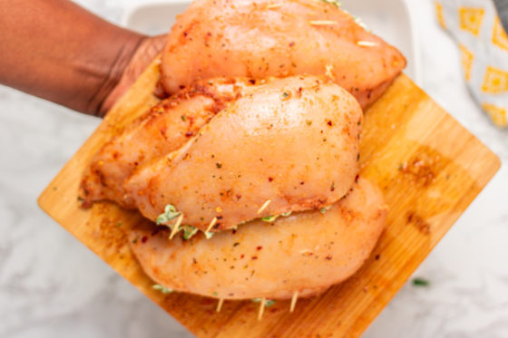 a hand holding a tray of uncooked chicken.