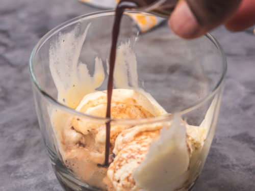 a hand pouring a brown drink over ice cream.