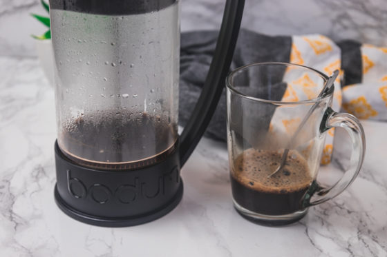 a glass of coffee and a french press