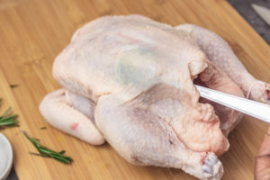 a spoon under the skin of a whole chicken.