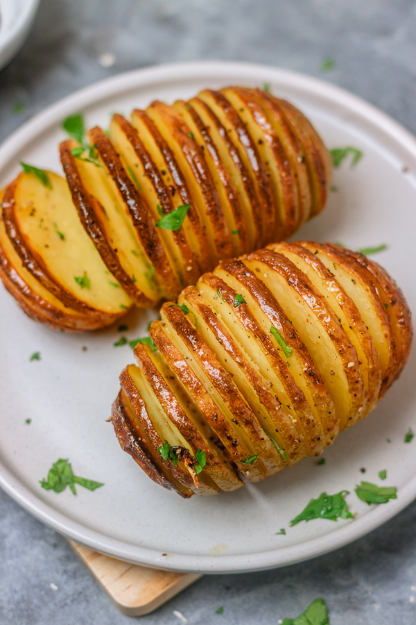 two baked potatoes on a plate garnished with chopped parsley.