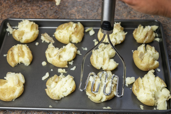 a hand pressing down on a cooked potato with a potato masher.