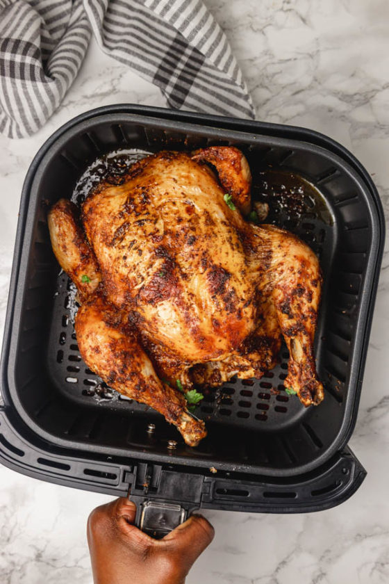 a hand holding a air fryer basket with chicken.