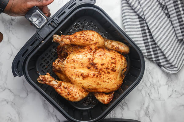 a hand holding air fryer basket containing a chicken.