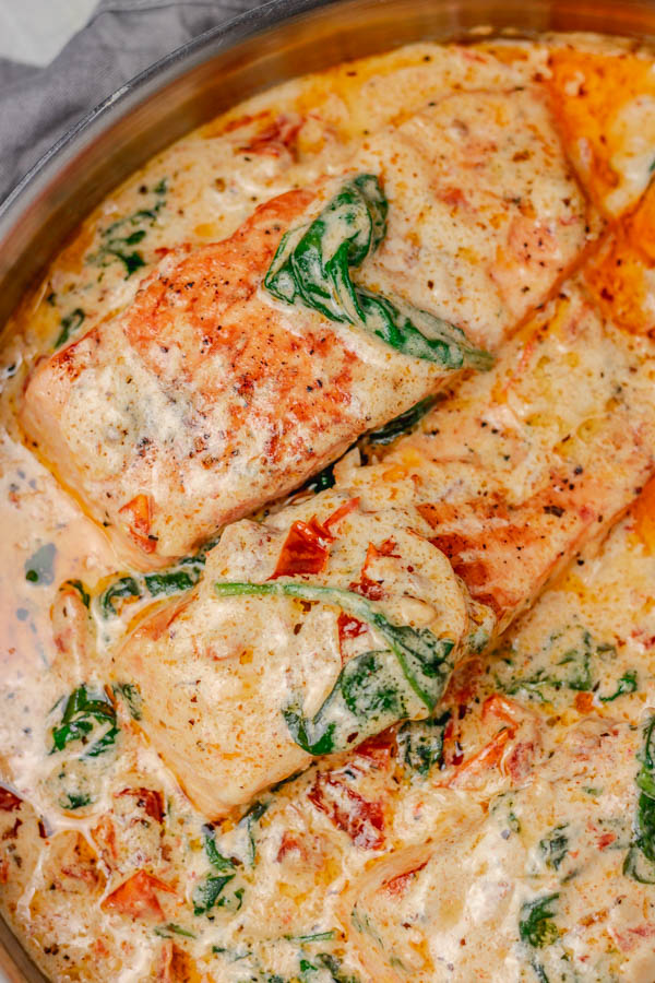 salmon fillets in a skillet of creamy sauce.