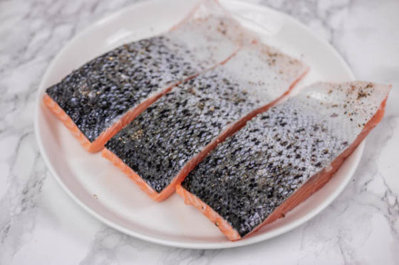 three raw salmon fillets on a plate.