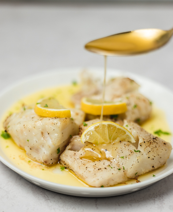 a hand pouring sauce on fish with a spoon.
